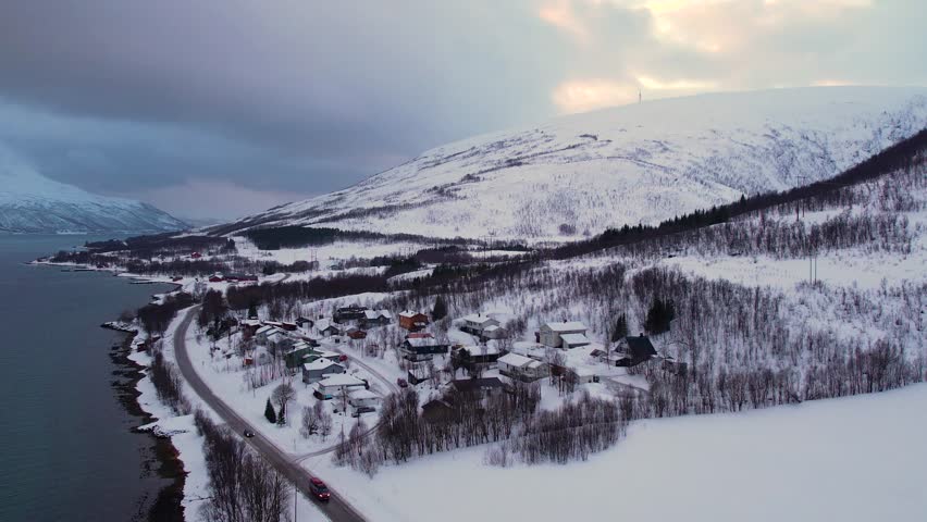 Snow covered mountain range on coastline in winter, Norway. Surroundings of town Tromso. Panoramic aerial view landscape of nordic snow cowered mountains, houses and ocean. Troms county, Fjordgard