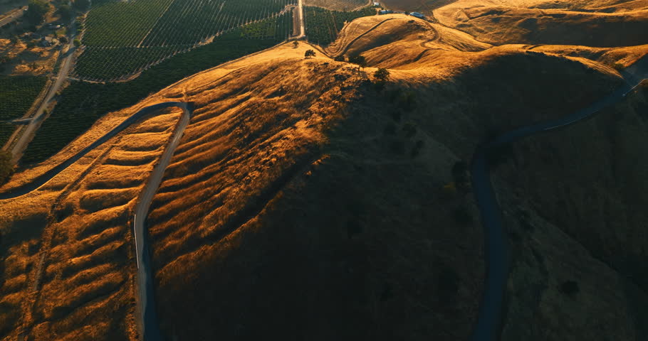 Going up over the rolled bare mount with a wavy highway on it. Green valley is at the foot of the mountains. Top view.