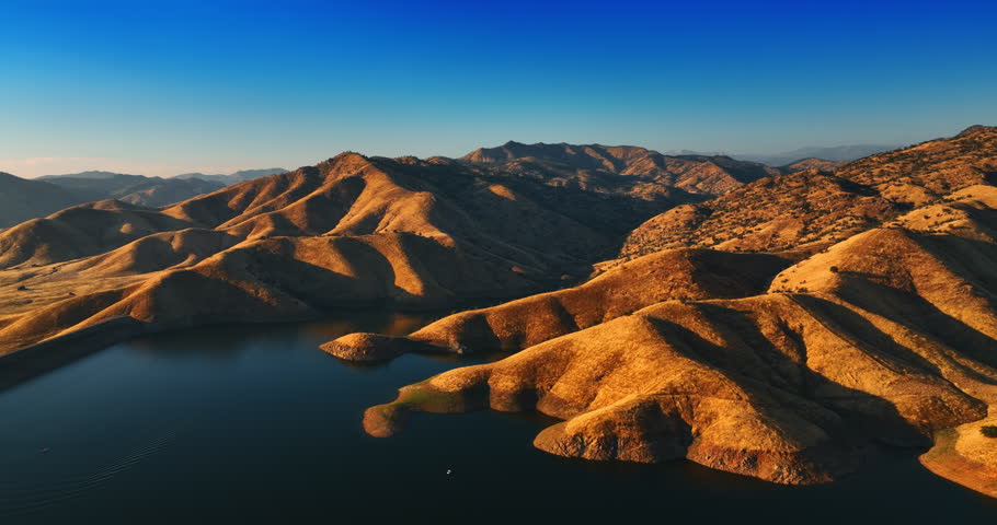 Slopes of bare brown mountains descending into the lake. Setting sun lighting the smooth rocks. California desert top view.