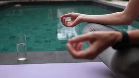 Woman sitting in lotus position near the swimming pool, close up of female hands
