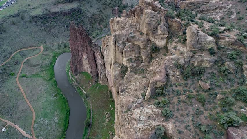 A drone shot of Smith Rock, Oregon, and a river that flows beside it. The camera starts above the rock facing down, then slowly tilts up, revealing Smith Rock and the land behind it.