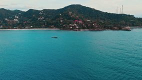 Dynamic round view to ship sailing among deep turquoise sea with green mountains background. Top view of breathtaking mountain landscape with tropical trees and inviting sea. Relaxing sea landscape