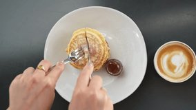 Tasty breakfast with pancakes and coffee. Woman cutting fluffy pancakes with maple syrup or honey during breakfast in a cafe