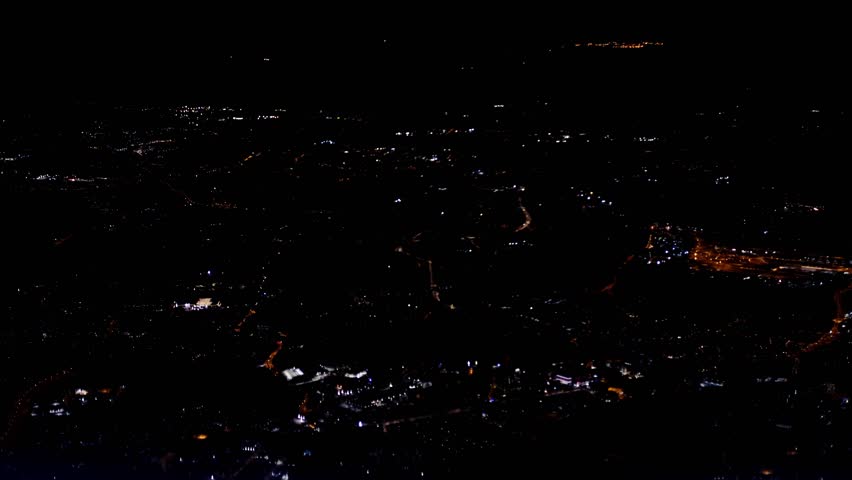 blurred view from window, porthole airplane, night city lights, roads glow shine sitting in dark, cityscape, transportation air passengers, tour tourism, landing of aircraft