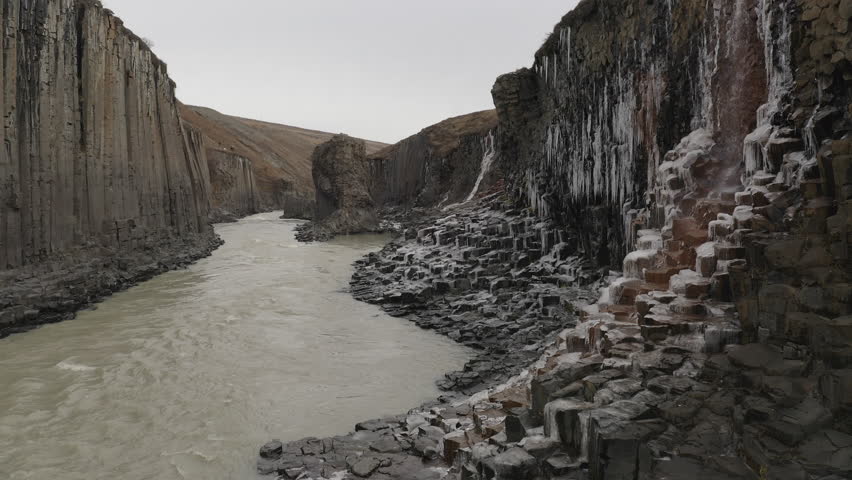 A canyon with red basaltic exagonal shapes with ice and a waterfall in Iceland in Iceland. Ethereal Landscapes in Ultra-HD 4K. Perfect for Wallpapers and Screensavers.