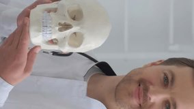 The doctor holds a human skull in his hands and smiles at the camera. Vertical video