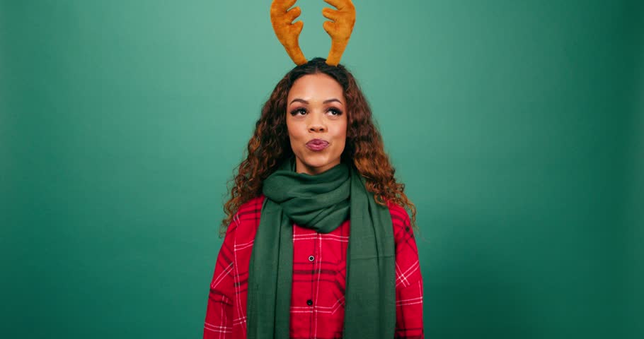 Excited young multi-ethnic woman covers eyes, Christmas reindeer studio
