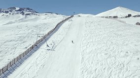 Slow motion aerial view of a person with skis on the descent of Farellones Park with a ski lift on the side, Chile.