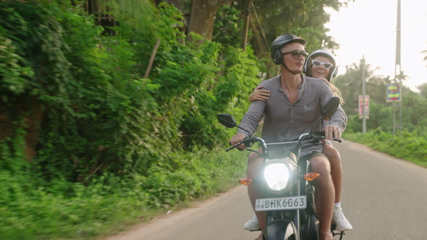 Happy couple ride on motorbike. Two lovers travel by motorcycle in tropics. Girlfriend, boyfriend drive scooter on jungle street. Travelers enjoy journey on bike. Man and woman in love on adventure.