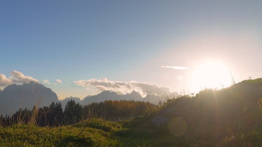 CLOSE UP, LENS FLARE: Agile young lady runs down the grassy hill with her doggo. They run fast and jump over small gaps on pathway. Great autumn sunny day for running in beautiful alpine environment.