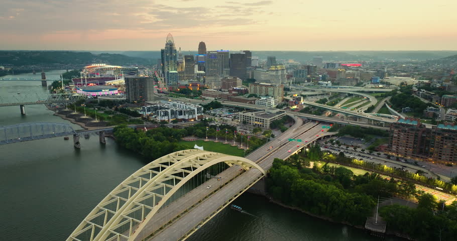 Driving cars on Daniel Carter Beard Bridge highway near illuminated high skyscraper buildings in downtown district of Cincinnati, Ohio, USA. American city with business financial district at sunset.