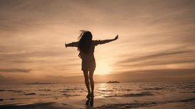 Silhouette of slim woman with arms raised up on beach at beautiful golden sea sunset. Happy young woman felling fun and free and jumping barefoot on beach at sunset at summer holidays - Powered by Shutterstock - Get 15% off with code: PIKWIZARD15