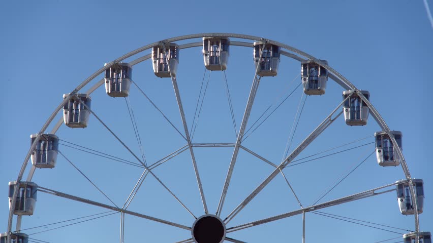 modern ferris wheel with closed cabins moving slowly at carnival amusement park with blue sky no clouds in the background illuminated wide angle close up shot at day and night time colorful lights Royalty-Free Stock Footage #1108722565
