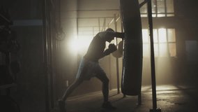 Alone boxer hits punching bag at dark gym in slow-motion. Young man training indoors. Strong athlete in gym - Powered by Shutterstock - Get 15% off with code: PIKWIZARD15