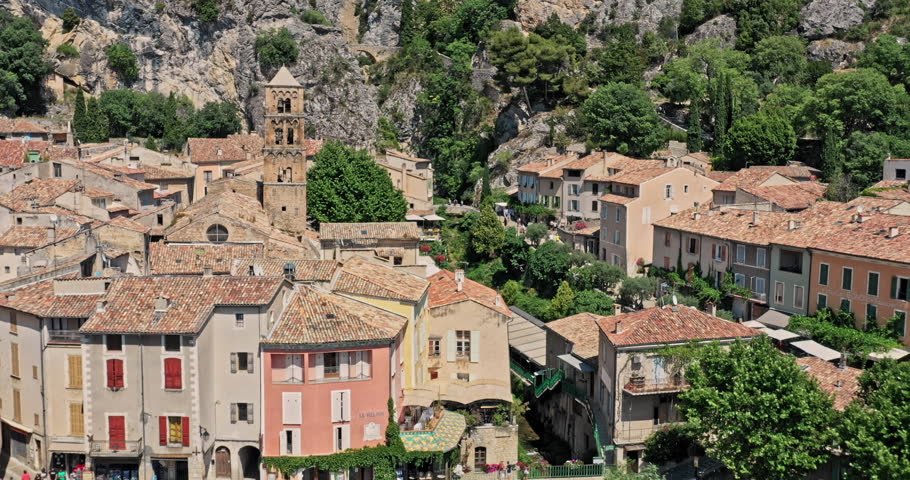 Moustiers Sainte Marie France Aerial v4 drone low reverse flyover medieval village town located at the foot of steep rock cut by a small ravine - July 2021
