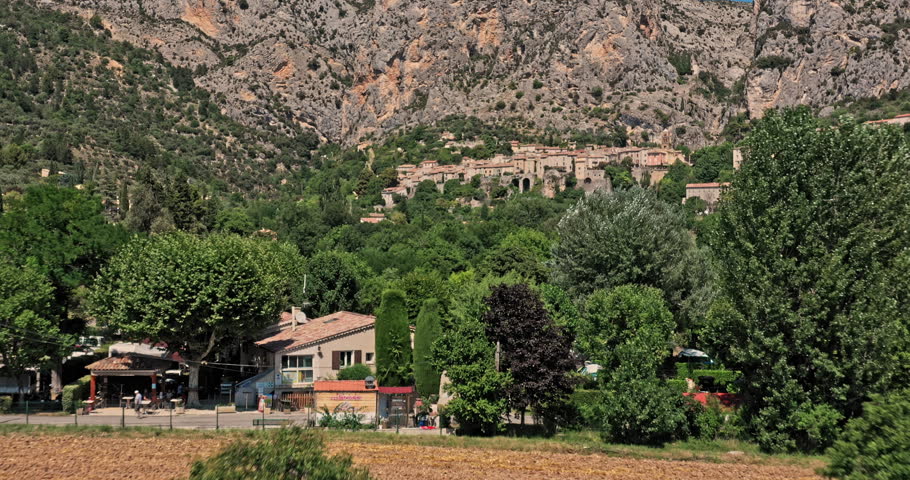 Moustiers Sainte Marie France Aerial v1 establishing shot low level drone flyover historic ancient village capturing beautiful townscape with medieval architecture toward rocky ravine - July 2021