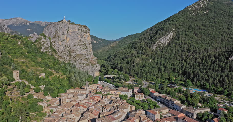 Castellane France Aerial v3 aerial dolly out shot away from clifftop chapelle notre dame du roc, capturing foothill village townscape with mountainous background against blue sky - July 2021