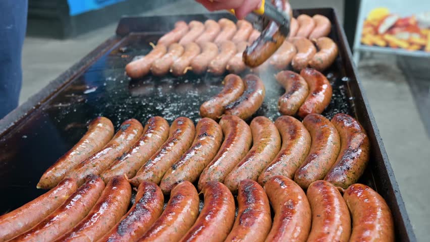 Close-up of sausages on the grill, male hand frying pork bratwurst for fast food barbeque.
