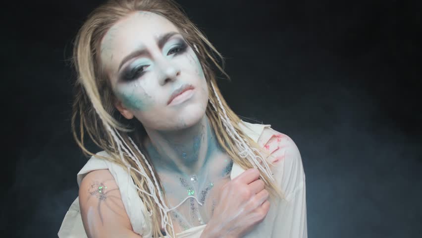 Halloween woman in makeup and a white shirt stained with blood in the studio on a black background.