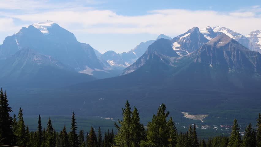 Views of the mountains of the Canadian Rockies from the top of the Lake Louise Gondola, Banff National Park, Alberta, Canada. Tall Rocky Mountains with snow, surrounded by lake and dense pine forests