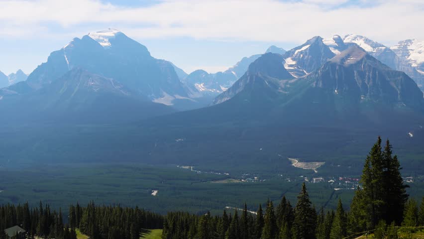 Views of the mountains of the Canadian Rockies from the top of the Lake Louise Gondola, Banff National Park, Alberta, Canada. Tall Rocky Mountains with snow, surrounded by lake and dense pine forests
