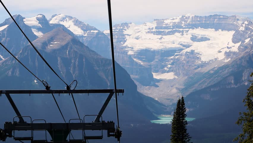 Views of the mountains of the Canadian Rockies from the top of the Lake Louise Gondola, Banff National Park, Alberta, Canada. Tall Rocky Mountains with snow, surrounded by lake and dense pine forests