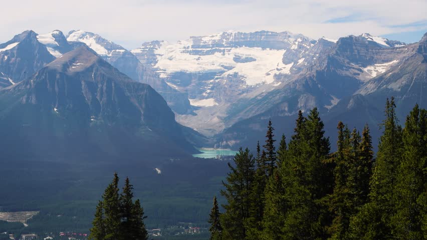 Views of the mountains of the Canadian Rockies from the top of the Lake Louise Gondola, Banff National Park, Alberta, Canada. Tall Rocky Mountains with snow, surrounded by lake and dense pine forests