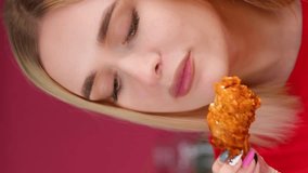 Vertical video. Young blonde woman eating a chicken wing.