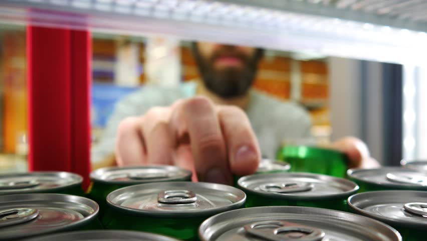 Close-up of many cans of energy drink or beer in the store fridge and a male buyer takes one