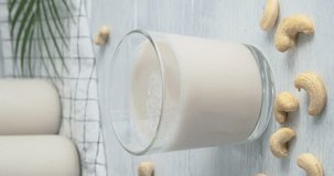 Cashew milk, person taking a glass of non-dairy drink made of cashew nuts from table, kitchen table on background, close-up video clip, 4k vertical footage, slow motion video, alternative vegan milk