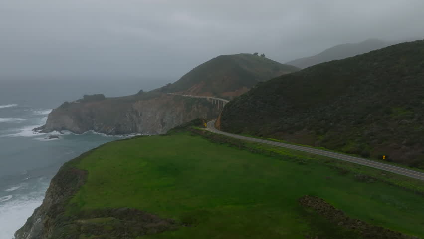 Aerial view of panoramic view winding in landscape along sea coast. Revealing beautiful high arch bridge. California, USA