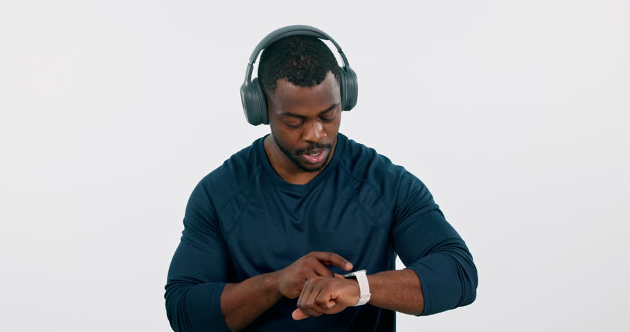 Fitness, music and smart watch with a sports black man in studio on a white background to track his health. Exercise, training and a workout app with a young athlete checking the time with headphones
