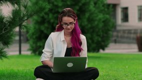 Portrait of pretty long-haired college girl with laptop preparing for exam while sitting on campus lawn. Charming young woman student in white shirt studying outside class in the park. - Powered by Shutterstock - Get 15% off with code: PIKWIZARD15
