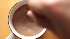 Person use a spoon to stir the coffee. Close-up top view a cup of coffee on wood table background. 