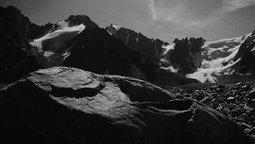 Stylised in an old archived style footage view of mountains with glaciers. 4K black and white video with noise and scratches effects.