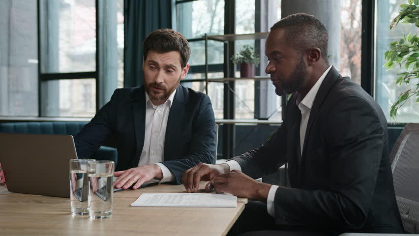 Diverse multiracial African American and Caucasian men colleagues coworkers businessmen financial agents discuss business project startup with laptop in office work with papers documents paperwork Royalty-Free Stock Footage #1108752823