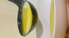 Vertical video. Cream soup is poured from a plastic black ladle into a white plate.