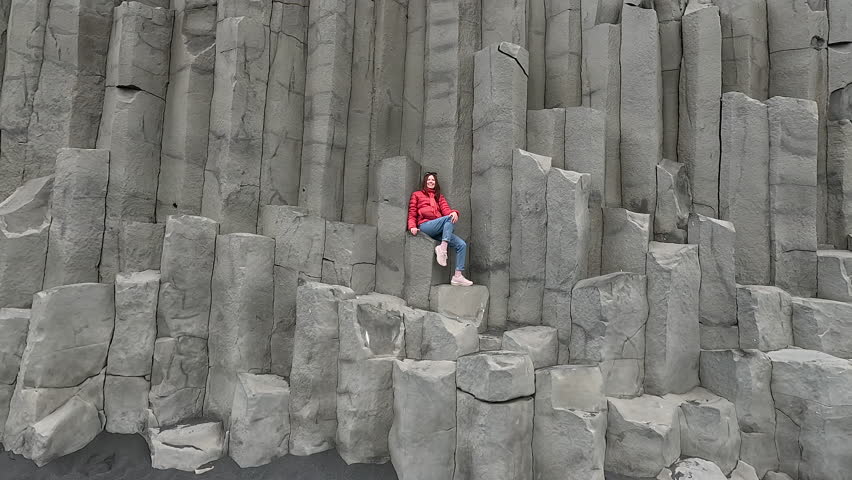 The girl sits on a rock on a black beach. Iceland.