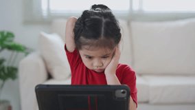 Asian child girl serious to looking using and touch tablet display screen. Baby smiling funny time to use tablet. Too much screen time. Cute girl watching videos while tv, Internet addiction concept.