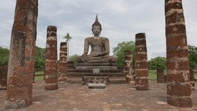 Slow motion video of big sitting buddha in ancient historic town of Sukhothai, remains of temples, World Heritage concept
