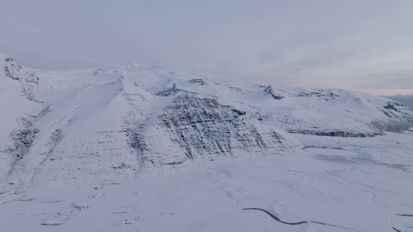 Aerial landscape view over Skaftafellsjokull glacier surrounding mountains, in Iceland, covered in snow, during sunset