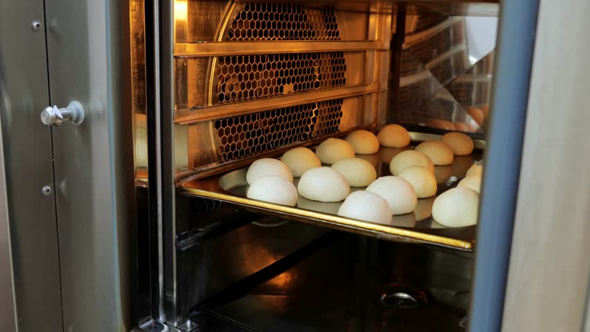The cook puts the dough in the oven, baking oven, preparation for baking buns, a small oven for baking. | Shutterstock HD Video #1108760081