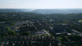 Drone-captured video reveals Staincliff, UK, with industrial buildings, bustling streets, Dewsbury General Hospital, and Yorkshire's morning landscape.
