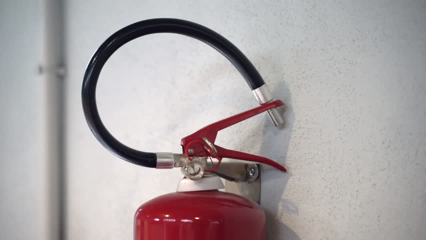 Close-up shot of fire extinguisher handle with nozzle hanging on white wall, extinguisher being used in fire emergency, obligatory equipment on industrial factories and other public institutions in Royalty-Free Stock Footage #1108765903