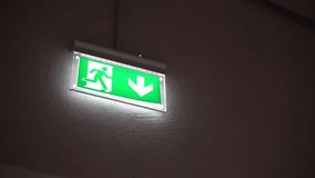 Illuminated emergency exit sign on the wall, down arrow and running person pointing the right direction to escape in case of danger, emergency exit symbol, direction for evacuation. High quality 4k - Powered by Shutterstock - Get 15% off with code: PIKWIZARD15
