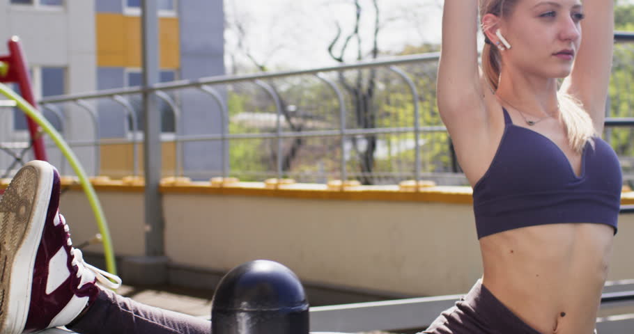 A young girl does a leg warm-up on the turnstile, a body warm-up on the sports ground in front of the house