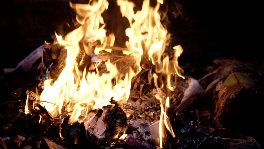 Slow motion speed of flames from burning trash outdoors at night. The collected household waste is burned in the backyard and produces a red and yellow dance of fire