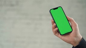 Close up of Phone With Green Screen Mock-Up In Men's Hands Against Background of White Wall