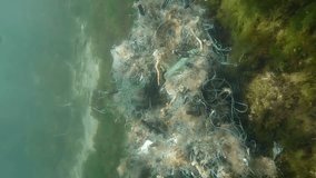 Vertical video, Lost fishing net lies on seabed in green algae Ulva in sun glare on shallow water, Around movement. Ghost gear, fishing gear that has been abandoned, lost or otherwise discarded