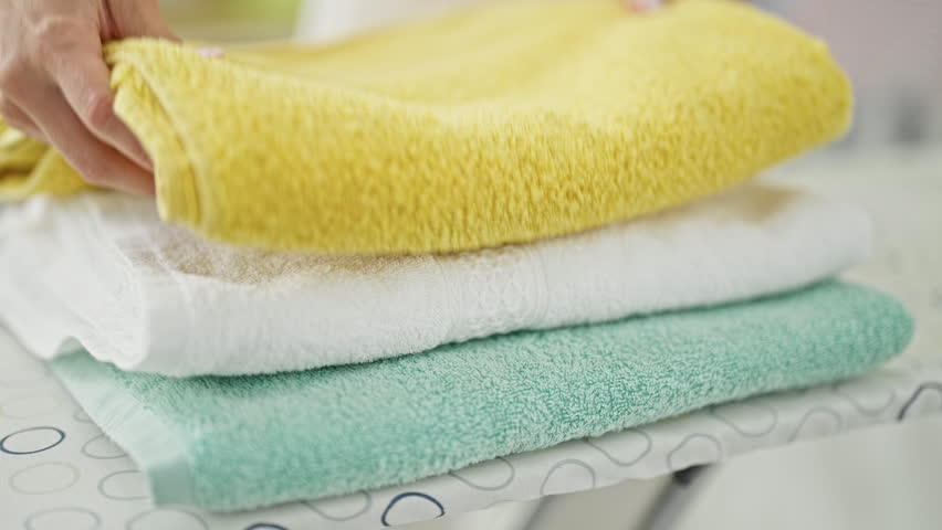 Young blonde woman folding towels at laundry room